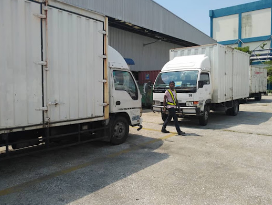 Commercial delivery trucks beside a logistics building, with a worker in a safety vest